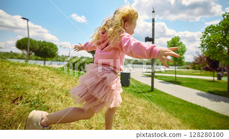 Side run glow. Joyful child running in park under clear blue sky 128280100