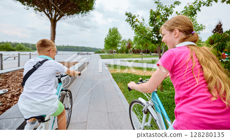 Wheels and words. Children cycling on scenic park pathway under cloudy sky 128280135