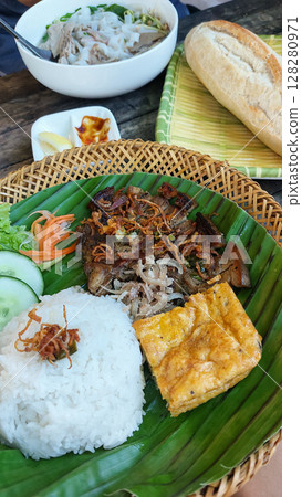 Trung chien or egg omelet, thit heo nuong xa or grilled pork chop and rice on a banana leaf, accompanied by pho bo or beef noodle soup and baguette. Authentic traditional Vietnamese cuisine 128280971