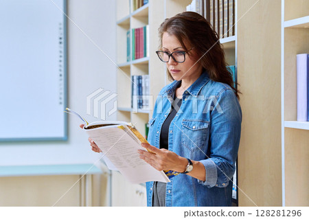 Portrait serious mature woman teacher, educational specialist reading textbook in classroom Portrait serious mature woman teacher, educational specialist reading textbook in classroom 128281296