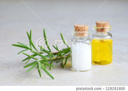 Rosemary essential oil in a small bottle and fresh twig on light background. Natural aroma cosmetic oil and salt 128281800