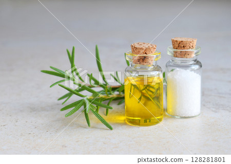 Rosemary essential oil in a small bottle and fresh twig on light background. Natural aroma cosmetic oil and salt 128281801