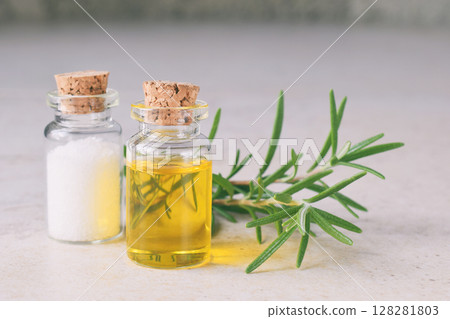 Rosemary essential oil in a small bottle and fresh twig on light background. Natural aroma cosmetic oil and salt 128281803