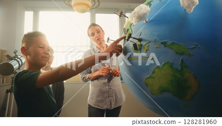 Boy Presenting Renewable Energy Sources Using Globe with 3D Models of Wind Turbines and Solar Panels 128281960