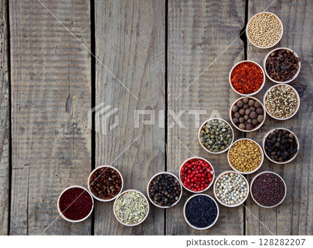 spices on a wooden background. Coriander, black pepper, paprika, mustard, turmeric, cumin, sumac, fenugreek, cloves, cubeb. 128282207
