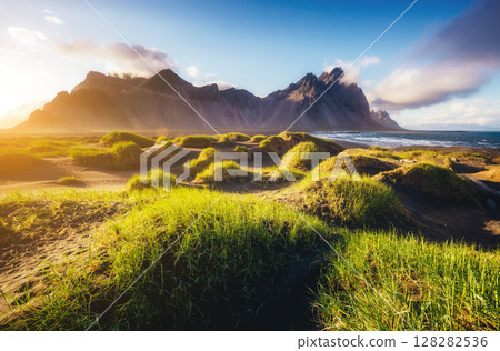 Beautiful view of the green hills glowing by sunlight. Location famous place Stokksnes cape, Vestrahorn (Batman Mountain), Iceland, Europe Beautiful view of the green hills glowing by sunlight. Location famous place Stokksnes cape, Vestrahorn (Batman Mountain), Iceland, Europe 128282536