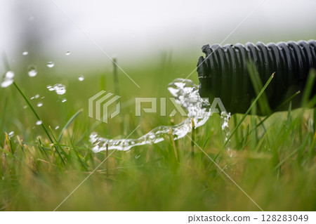 Residential sump pump drain line discharging water into grass yard after a rainstorm Residential sump pump drain line discharging water into grass yard after a rainstorm 128283049