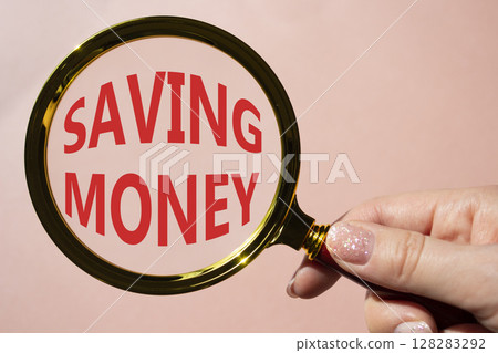 Saving Money symbol. Concept words Saving Money on magnifying glass. Businessman hand. Beautiful pink background. Business and Saving Money concept. Copy space. 128283292