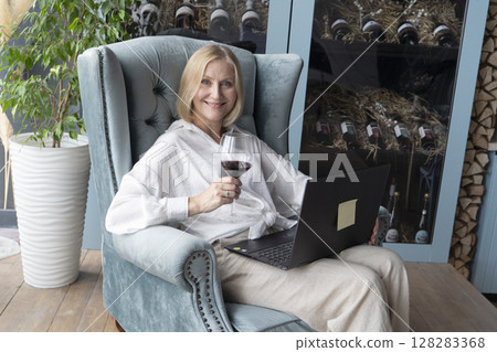 An Elegant Woman Joyfully Toasting with a Glass of Rich Red Wine in a Beautifully Stylish Kitchen Space 128283368