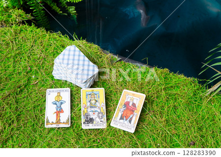 A beautiful arrangement of Tarot cards spread out on soft grass next to a peaceful and tranquil water body A beautiful arrangement of Tarot cards spread out on soft grass next to a peaceful and tranquil water body 128283390