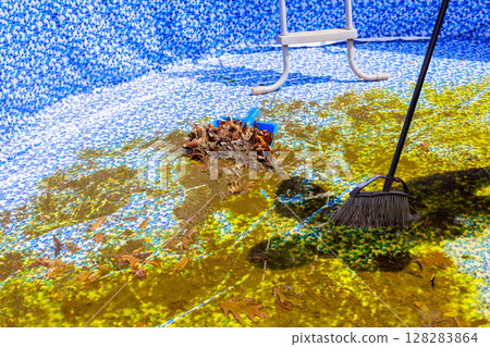 Manual labor is being done to remove leaves muck from stagnant swimming pool on works day. 128283864