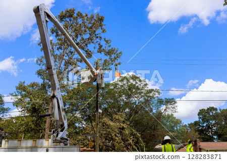 Utility workers use cherry picker to restore power lines damaged by recent storms in suburban neighborhood. 128283871