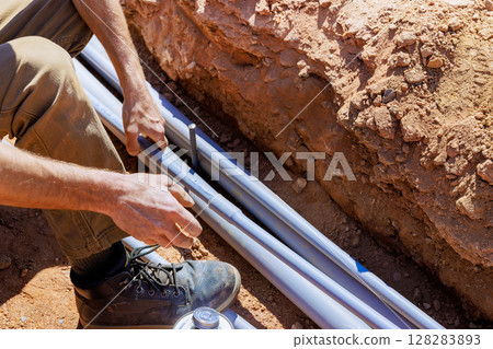 Construction worker laying electrical pipes in trench under works day 128283893
