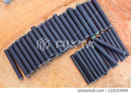 Black rubber pipes meticulously lined up at construction site, ready for installation after transport. Black rubber pipes meticulously lined up at construction site, ready for installation after transport. 128283909