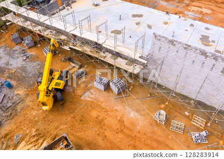 Heavy machinery works on construction site with materials scaffolding in place under works day Heavy machinery works on construction site with materials scaffolding in place under works day 128283914