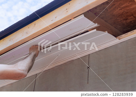 Worker is carefully placing new soffit siding panels under eaves of house Worker is carefully placing new soffit siding panels under eaves of house 128283939