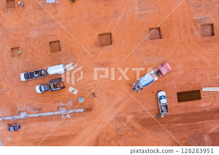 Workers operate machinery prepare the site for building foundations in an expansive, open area. 128283951