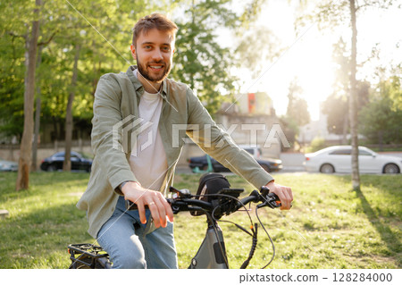 Young man enjoys sunny day in park while riding bicycle near trees and greenery during warm afternoon Young man enjoys sunny day in park while riding bicycle near trees and greenery during warm afternoon 128284000