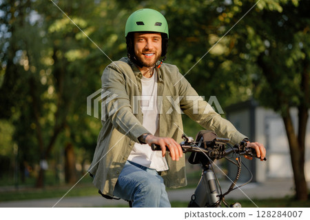 Smiling man rides bicycle wearing helmet in park during sunny day Smiling man rides bicycle wearing helmet in park during sunny day 128284007