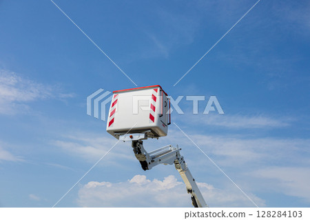 A tall work platform is lifted high, showcasing its reach against a bright, sunny sky with scattered clouds 128284103