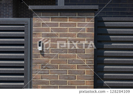 An intercom is mounted on a stylish brick wall at the entrance of a contemporary home, providing communication access for visitors An intercom is mounted on a stylish brick wall at the entrance of a contemporary home, providing communication access for visitors 128284109