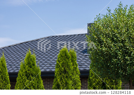 Slate roofing tiles cover a well-maintained rooftop, surrounded by tall green trees under a bright blue sky in a cozy neighborhood 128284118