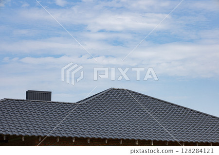 Metallic roofing features a sleek tiled design, reflecting sunlight under a clear blue sky at a construction site during daylight hours 128284121