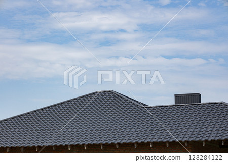 An elevated view of a stylish tiled roof construction on a house, showcasing the roofing materials against a bright blue sky An elevated view of a stylish tiled roof construction on a house, showcasing the roofing materials against a bright blue sky 128284122