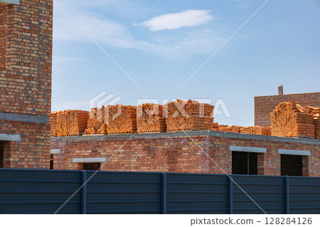 Workers prepare a construction site with new brick structures, with stacks of bricks visible against a bright blue sky 128284126