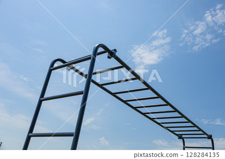 Gymnast engages in strength training on horizontal parallel bars under a clear blue sky, highlighting dedication to fitness and health Gymnast engages in strength training on horizontal parallel bars under a clear blue sky, highlighting dedication to fitness and health 128284135