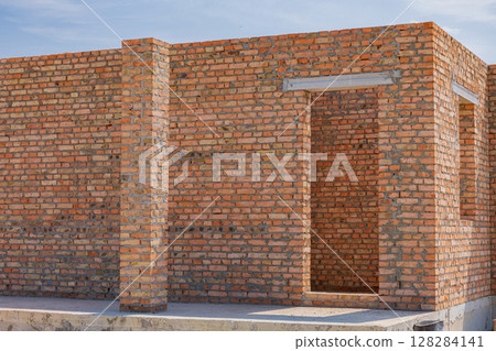 Construction of a brick structure is underway, showcasing raw, unfinished walls and an open doorway in bright sunlight 128284141