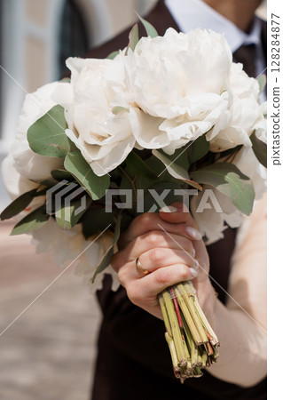 Elegant Wedding Bouquet with White Peonies and Eucalyptus Held by a Groomsman in Traditional Formal Attire, Soft Lighting Elegant Wedding Bouquet with White Peonies and Eucalyptus Held by a Groomsman in Traditional Formal Attire, Soft Lighting 128284877