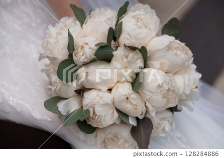 Elegant Ivory Peony Bridal Bouquet with Eucalyptus Accents. Close-Up Wedding Flowers, Soft White Blooms, Lace Dress Detail, Rustic Style. 128284886