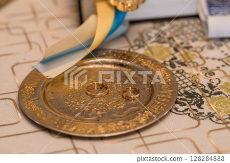 Orthodox Wedding Rings on Paten during Ceremony with Intricate Embroidery, Gold Chalice, Rich Textures, and Religious Symbolism in Soft Lighting. Orthodox Wedding Rings on Paten during Ceremony with Intricate Embroidery, Gold Chalice, Rich Textures, and Religious Symbolism in Soft Lighting. 128284888