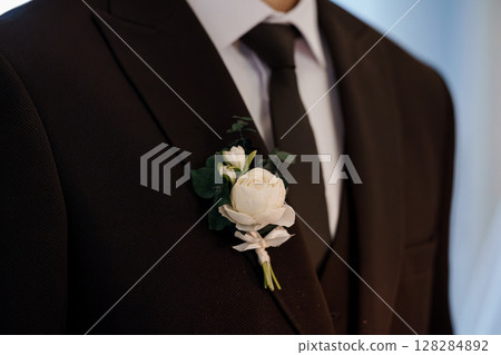 Elegant Groom Boutonniere Detail: Black Suit Lapel with Cream Rose, Eucalyptus, Ribbon, Wedding Formal Wear, Close-Up Fashion Photography. Elegant Groom Boutonniere Detail: Black Suit Lapel with Cream Rose, Eucalyptus, Ribbon, Wedding Formal Wear, Close-Up Fashion Photography. 128284892