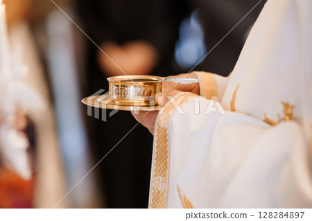 Eucharistic Celebration: Priest Holding Golden Chalice and Paten During Holy Communion Ceremony in Church, Bright Vestments. 128284897