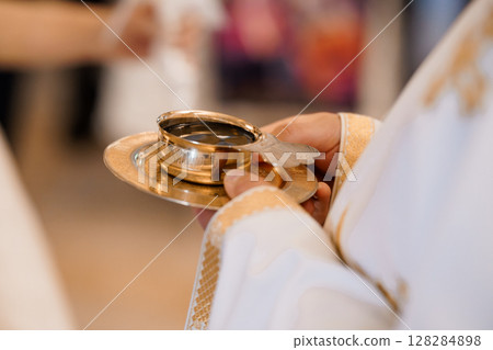 Catholic Eucharist Ceremony: Priest Presenting Golden Chalice with Wine During Holy Communion Rite, Blurred Church Interior, Warm Lighting 128284898