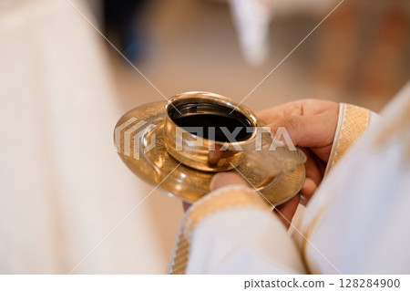 Sacred Eucharist Ritual: Golden Chalice Holding Wine, Christian Priest's Hands, Cream Altar Cloth, Liturgical Celebration, Warm Golden Light 128284900