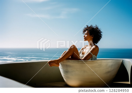 A woman is sitting in a large white bowl on a balcony overlooking the ocean 128284950