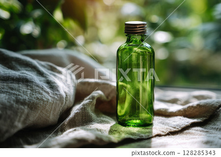 Green glass bottle with metal cap standing on soft linen fabric 128285343