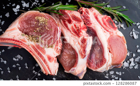 The photo of sliced lamb carcass on black marble with sea salt crumbs and rosemary sprig 128286087