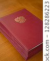 An Elegant Red Bound Volume Displayed with a Golden Emblem on a Beautiful Wooden Table 128286223
