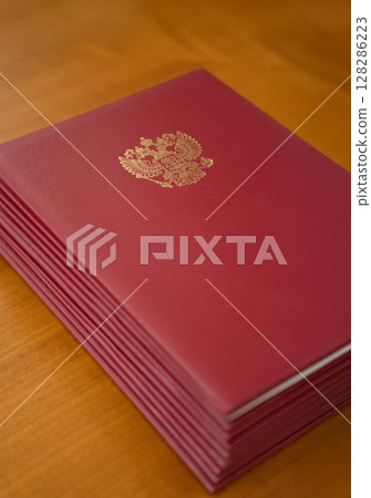 An Elegant Red Bound Volume Displayed with a Golden Emblem on a Beautiful Wooden Table 128286223
