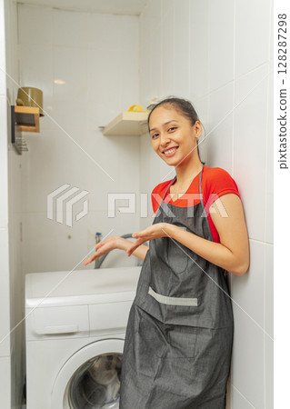 A Happy Smiling Woman Showcasing a Washing Machine in a Modern Laundry Room 128287298