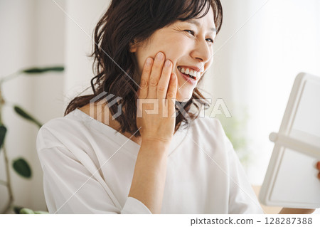 一位 50 多歲的中年婦女看著鏡子裡的皮膚微笑 一位 50 多歲的中年婦女看著鏡子裡的皮膚微笑 128287388