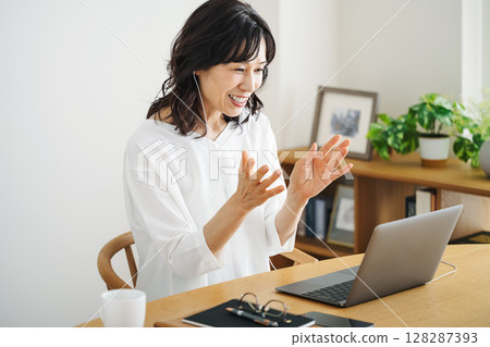 一位 50 多歲的中年女性正在家中客廳召開線上會議 128287393