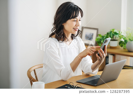 A middle-aged woman in her 50s looking at her smartphone in the living room at home A middle-aged woman in her 50s looking at her smartphone in the living room at home 128287395