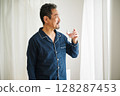 一名 50 多歲的中年男子早上起床後穿著睡衣喝了一杯水 128287453