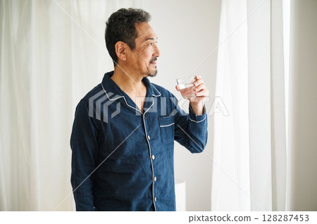 A middle-aged man in his 50s drinking a glass of water in his pajamas after waking up in the morning A middle-aged man in his 50s drinking a glass of water in his pajamas after waking up in the morning 128287453