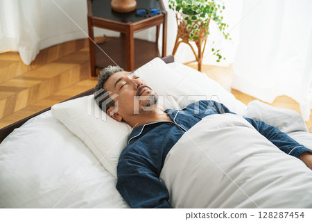 一名 50 多歲的中年男子在臥室的床上睡覺 一名 50 多歲的中年男子在臥室的床上睡覺 128287454